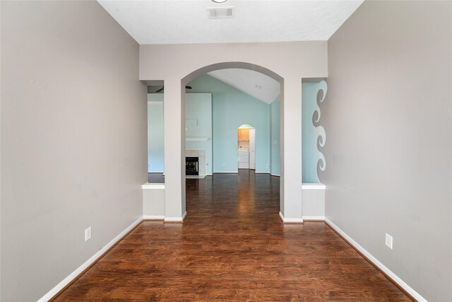 hallway featuring wood finished floors, visible vents, baseboards, arched walkways, and vaulted ceiling