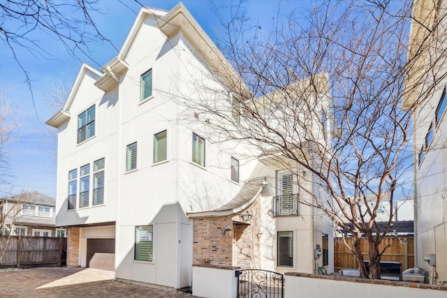 view of front of home with a fenced front yard, a garage, brick siding, decorative driveway, and stucco siding