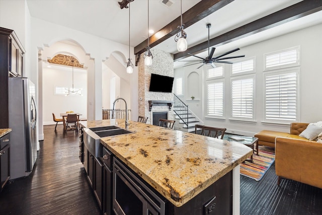 kitchen with a kitchen island with sink, a fireplace, a sink, open floor plan, and appliances with stainless steel finishes