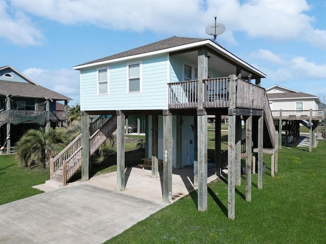 rear view of property featuring roof with shingles, a yard, covered porch, a carport, and stairs
