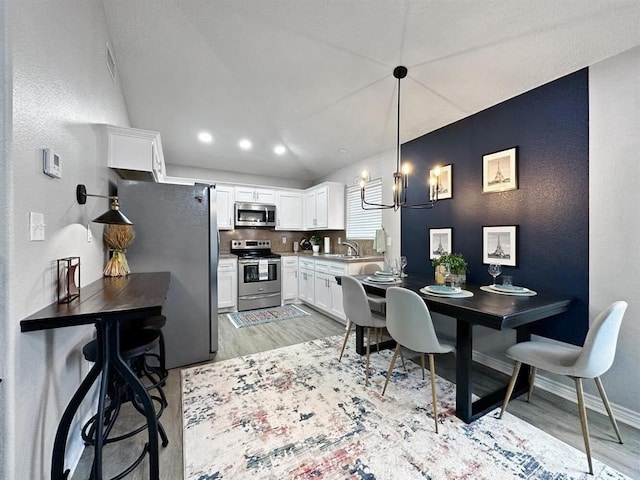 kitchen featuring stainless steel appliances, a sink, white cabinets, light countertops, and decorative light fixtures