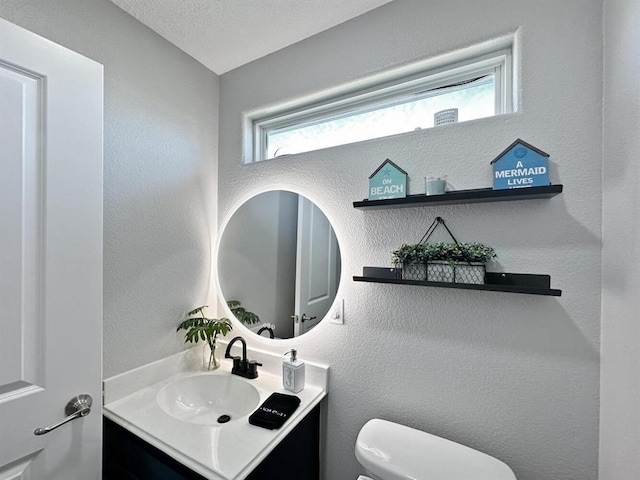 half bathroom with toilet, a textured wall, and vanity