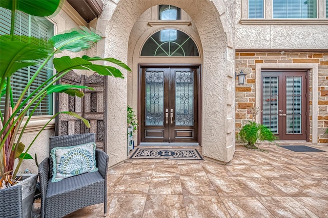 property entrance featuring stone siding, french doors, and stucco siding