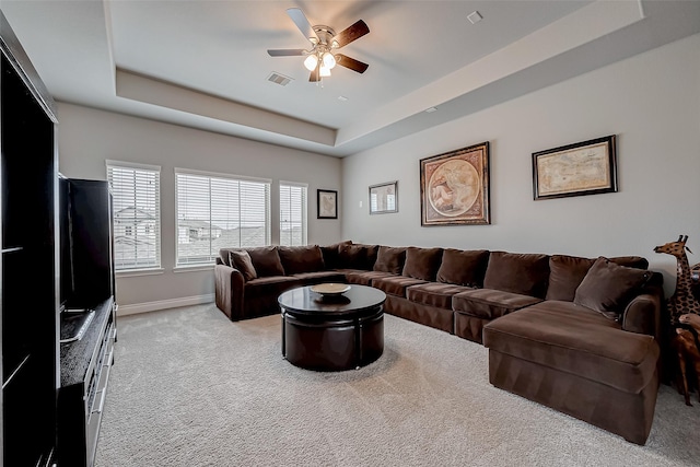 living room with a raised ceiling, light colored carpet, visible vents, ceiling fan, and baseboards