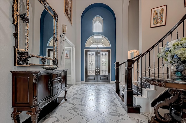 entrance foyer featuring arched walkways, a high ceiling, marble finish floor, french doors, and stairway