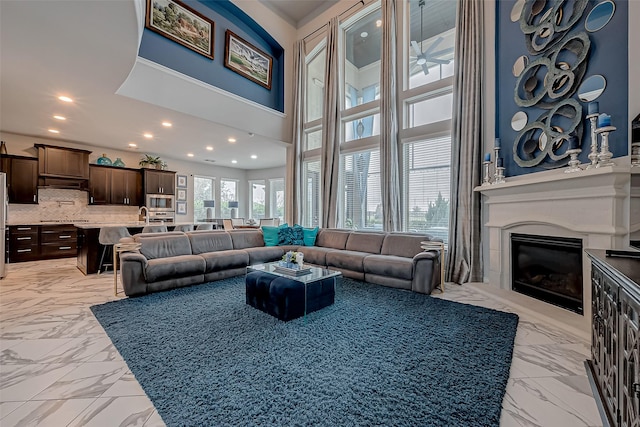 living room with a towering ceiling, marble finish floor, recessed lighting, and a glass covered fireplace