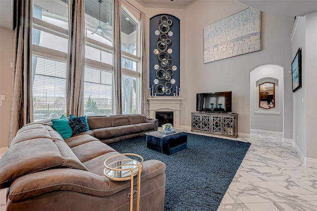 living room with arched walkways, a towering ceiling, baseboards, marble finish floor, and a glass covered fireplace