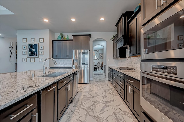 kitchen featuring marble finish floor, stainless steel appliances, decorative backsplash, a sink, and light stone countertops