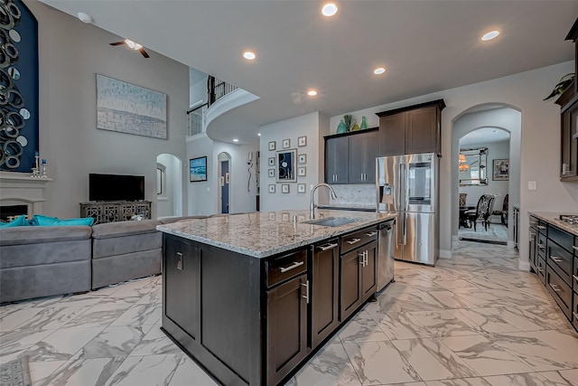 kitchen with stainless steel appliances, arched walkways, a center island with sink, and a sink