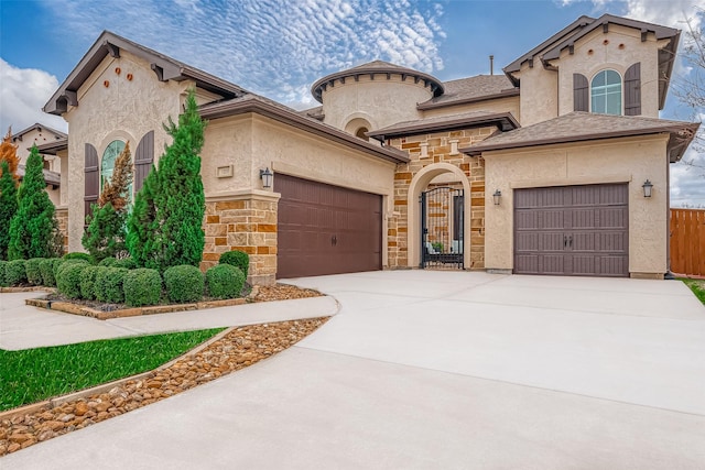 mediterranean / spanish-style house featuring a garage, concrete driveway, stone siding, fence, and stucco siding