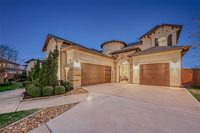 mediterranean / spanish home featuring stone siding, an attached garage, concrete driveway, and stucco siding