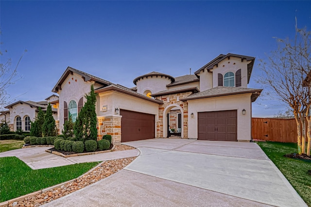 mediterranean / spanish house with stucco siding, concrete driveway, fence, a garage, and stone siding