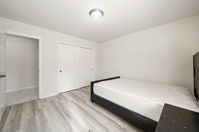 unfurnished bedroom featuring light wood finished floors, baseboards, and a closet