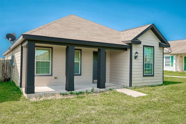 back of property with roof with shingles, a yard, and a patio