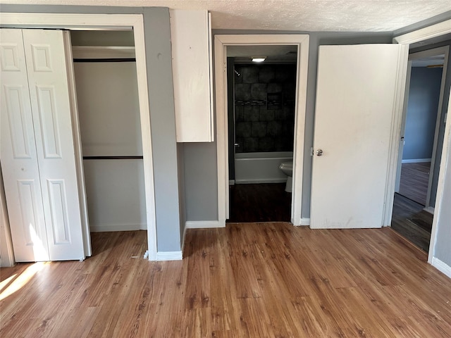 unfurnished bedroom with a closet, a textured ceiling, baseboards, and wood finished floors