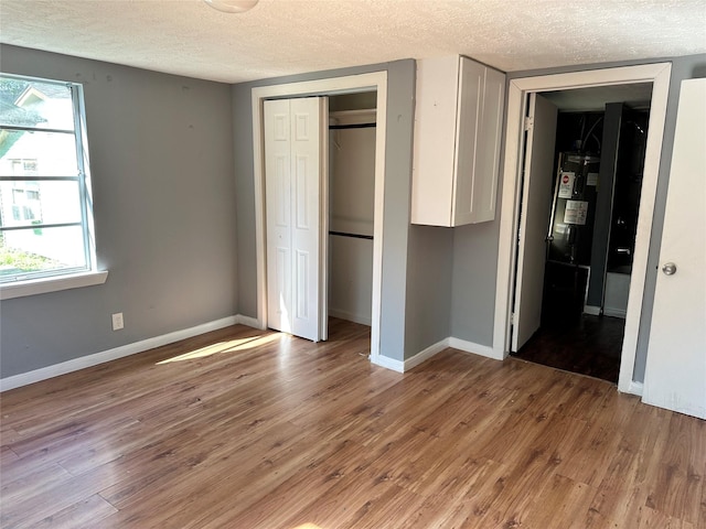 unfurnished bedroom featuring a textured ceiling, a closet, baseboards, and light wood-style floors