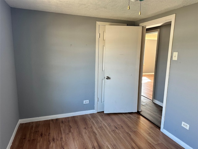 unfurnished bedroom featuring a textured ceiling, baseboards, and wood finished floors