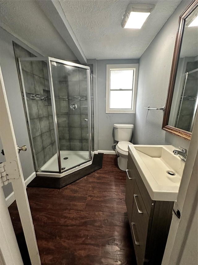 bathroom with a textured ceiling, wood finished floors, vanity, baseboards, and a stall shower