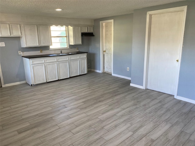 kitchen featuring light wood finished floors, baseboards, dark countertops, a textured ceiling, and a sink