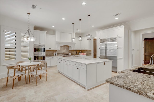 kitchen featuring stainless steel appliances, hanging light fixtures, a kitchen island with sink, and white cabinetry