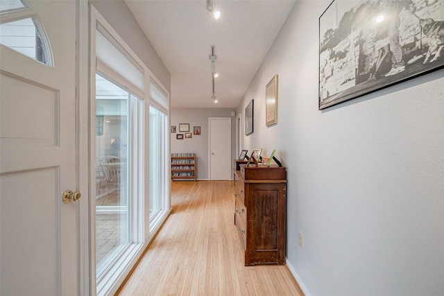 hall with light wood-type flooring, a healthy amount of sunlight, baseboards, and track lighting