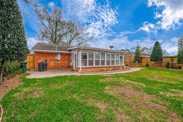 rear view of house with a fenced backyard, brick siding, a sunroom, a lawn, and a patio area