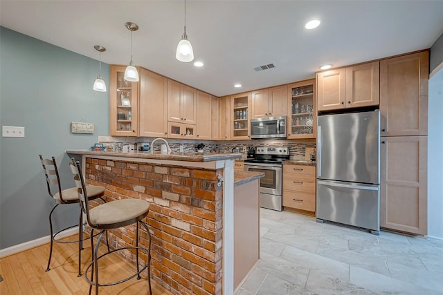 kitchen featuring visible vents, stainless steel appliances, light brown cabinetry, and glass insert cabinets