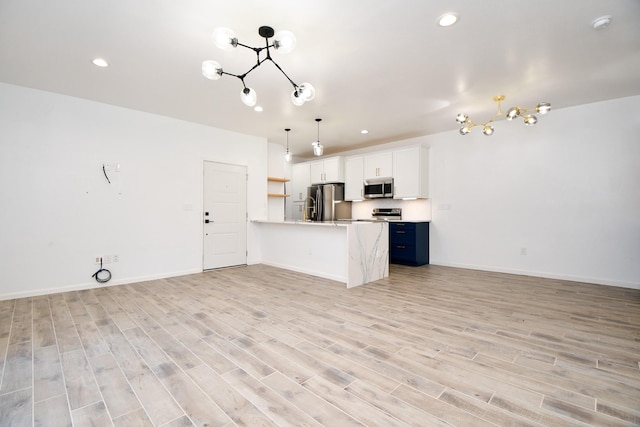 kitchen with stainless steel appliances, white cabinetry, open floor plan, hanging light fixtures, and light countertops