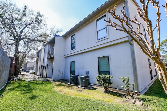 rear view of property featuring a yard, stucco siding, fence, and central air condition unit