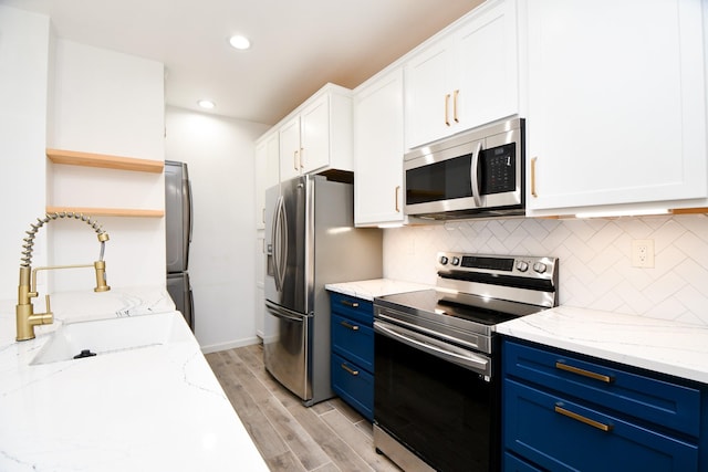 kitchen with stainless steel appliances, a sink, white cabinets, blue cabinetry, and open shelves