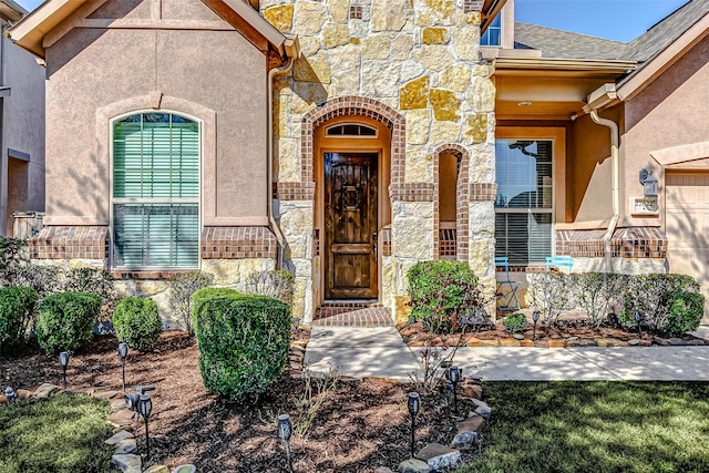 view of exterior entry featuring stone siding, a shingled roof, and stucco siding