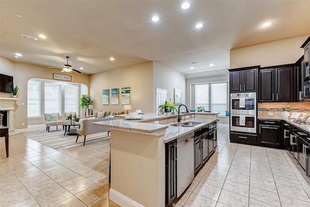 kitchen featuring an island with sink, light stone counters, appliances with stainless steel finishes, open floor plan, and a sink