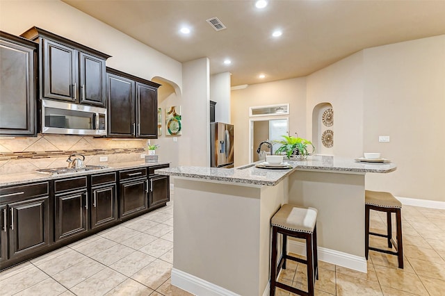 kitchen with a center island with sink, stainless steel appliances, visible vents, backsplash, and a kitchen bar