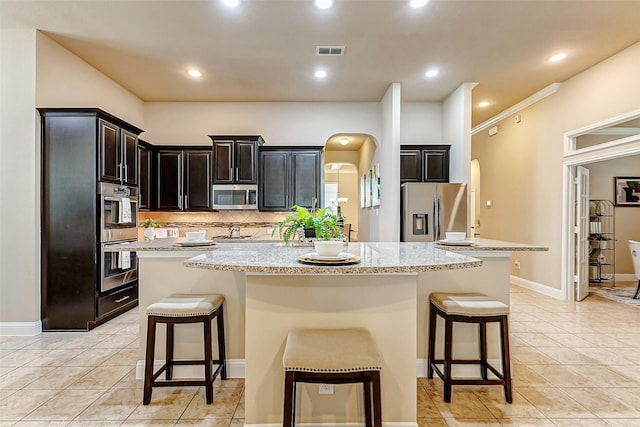 kitchen with visible vents, arched walkways, a kitchen island, appliances with stainless steel finishes, and light stone countertops