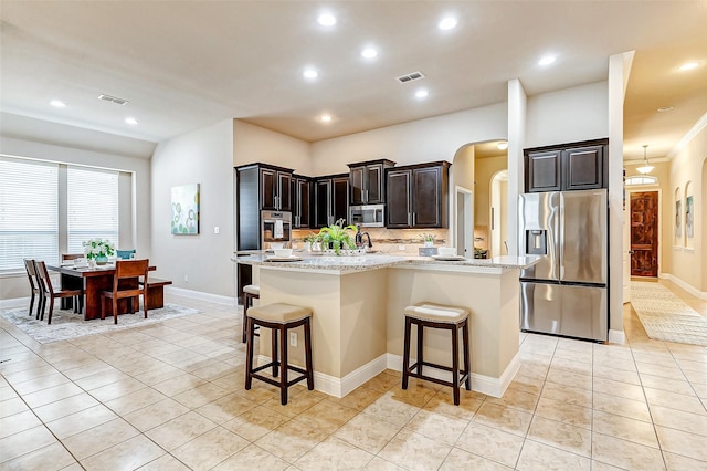 kitchen featuring arched walkways, stainless steel appliances, a center island with sink, and a kitchen breakfast bar