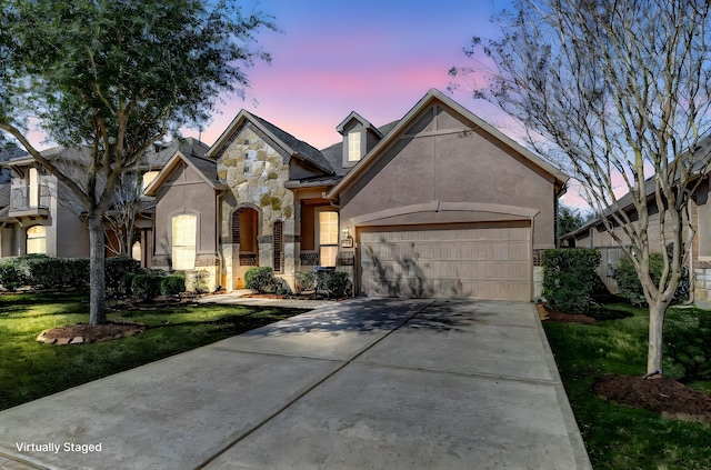 view of front of house with a yard, stucco siding, an attached garage, stone siding, and driveway