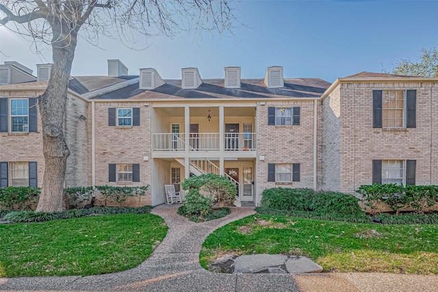 view of front of property with a front yard, brick siding, ceiling fan, and a balcony