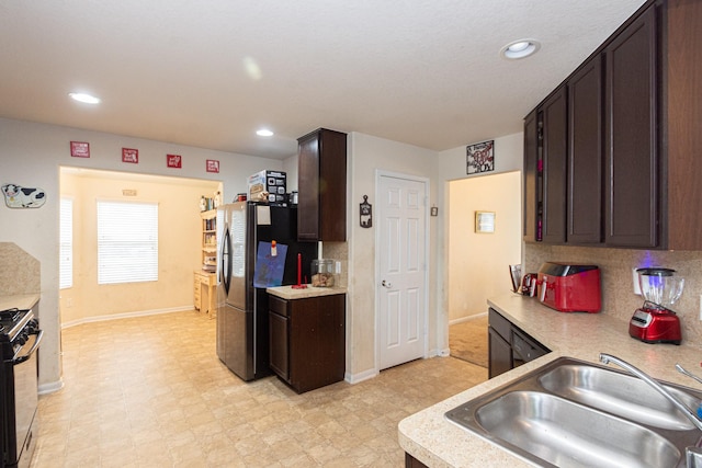 kitchen with dark brown cabinetry, a sink, light countertops, freestanding refrigerator, and gas range oven