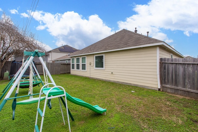 back of property with a fenced backyard, a lawn, a playground, and roof with shingles