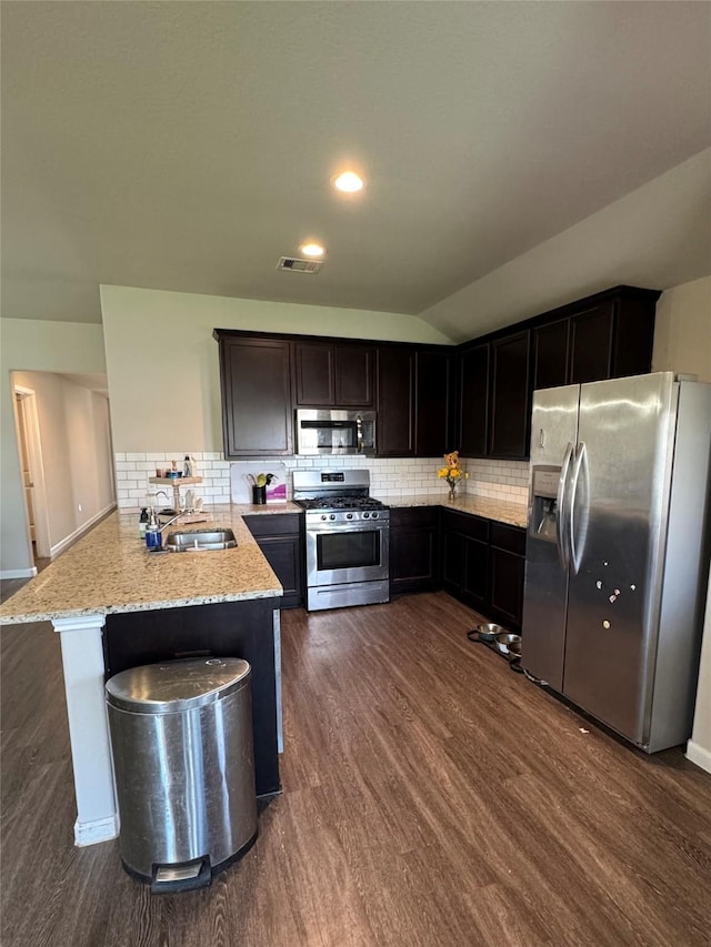 kitchen with tasteful backsplash, appliances with stainless steel finishes, dark wood-type flooring, a peninsula, and a sink