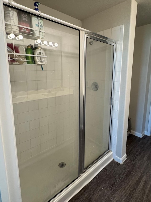 full bath with a shower stall, baseboards, and wood finished floors