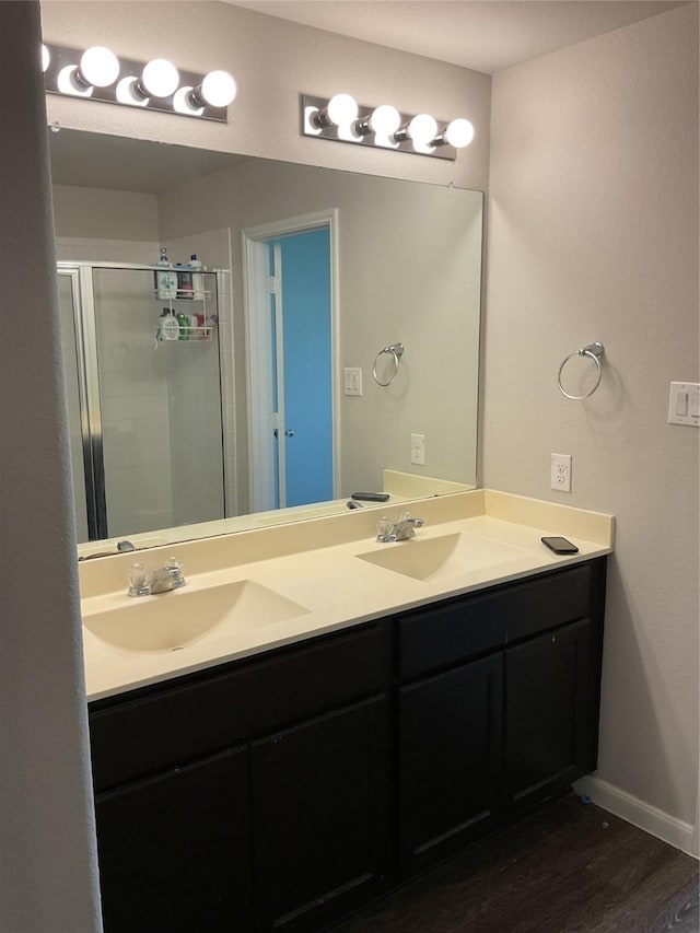 bathroom with double vanity, wood finished floors, a stall shower, and a sink