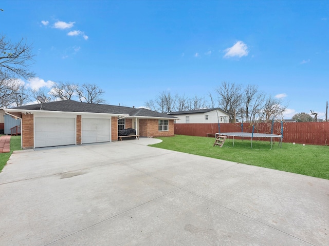 ranch-style home with a trampoline, concrete driveway, an attached garage, a front yard, and fence