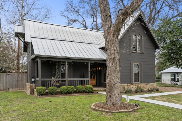 view of front facade with a porch, a standing seam roof, fence, metal roof, and a front lawn