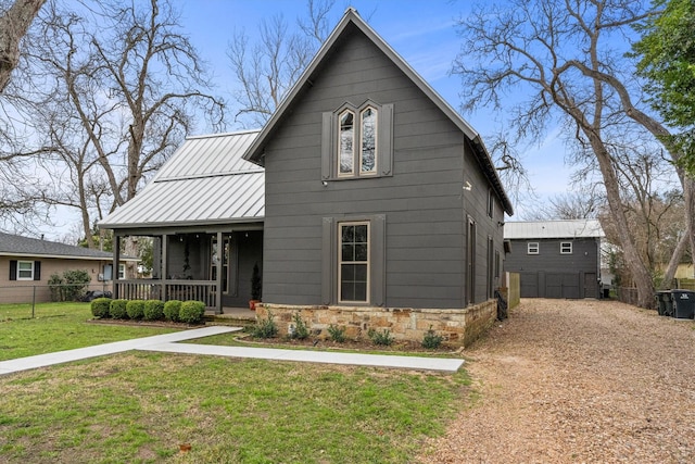 view of front of property featuring dirt driveway, a porch, a standing seam roof, stone siding, and a front lawn