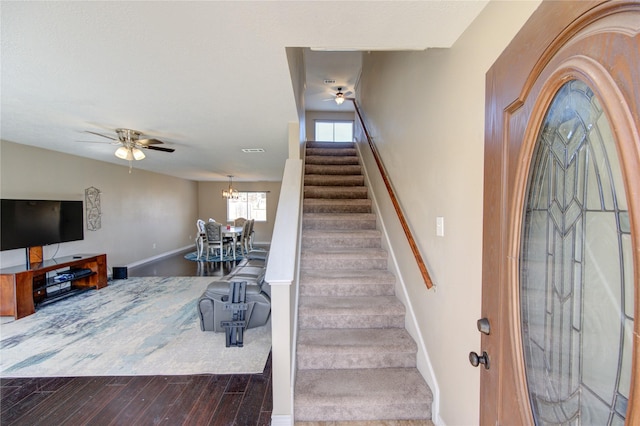 foyer entrance featuring baseboards, stairway, dark wood-style flooring, and ceiling fan with notable chandelier