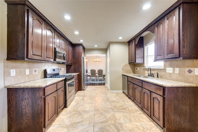 kitchen with dark brown cabinetry, appliances with stainless steel finishes, light stone counters, and a sink