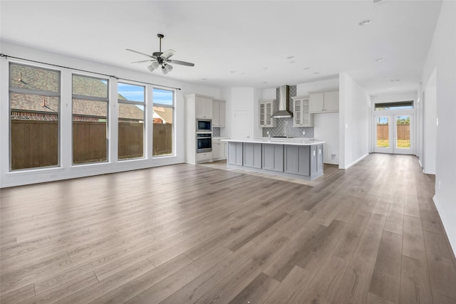 unfurnished living room with light wood-style floors, a ceiling fan, and french doors