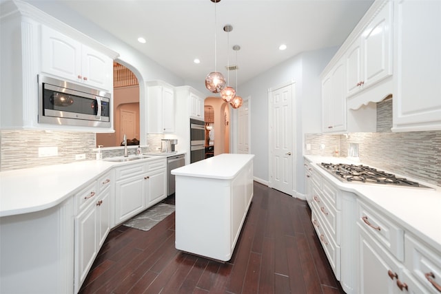 kitchen with arched walkways, appliances with stainless steel finishes, dark wood-type flooring, a sink, and a kitchen island