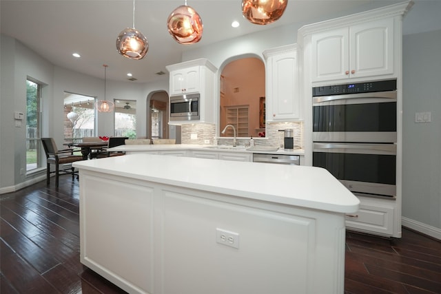 kitchen with arched walkways, stainless steel appliances, tasteful backsplash, white cabinets, and a sink